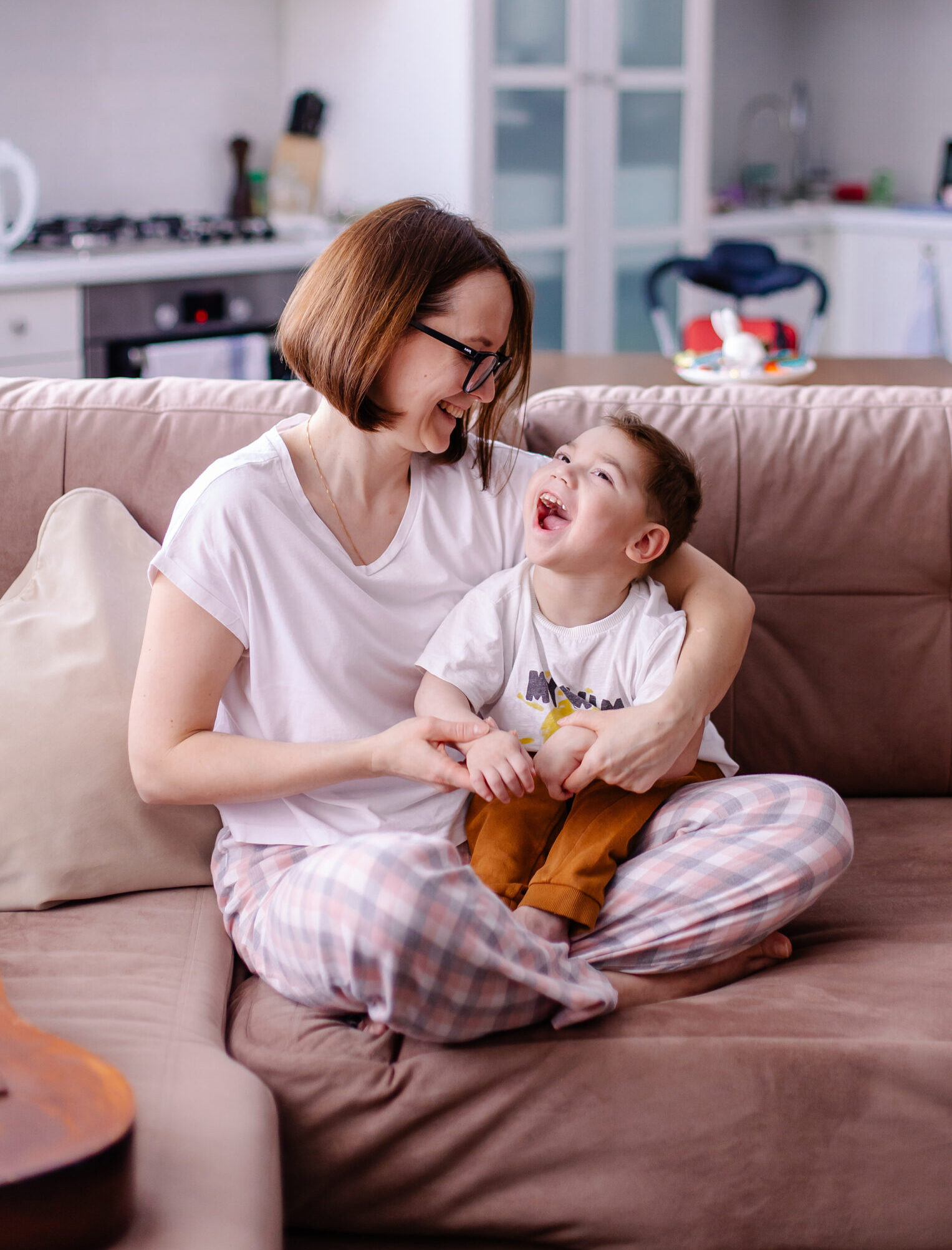 Parent caregiver sitting on couch holding young son with cerebral palsy.