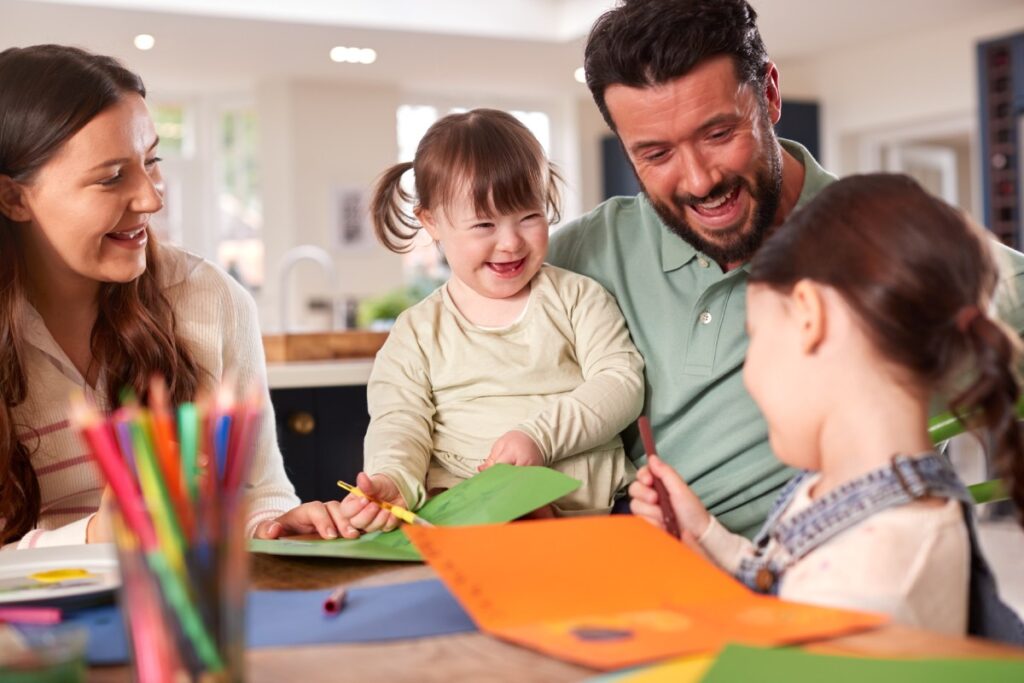 Mom, dad and two young sisters sitting at kitchen table coloring with markers.