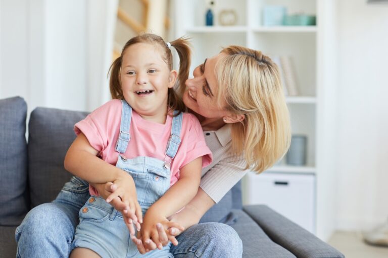 young girl with intellectual disability smiling sitting on mom's lap.