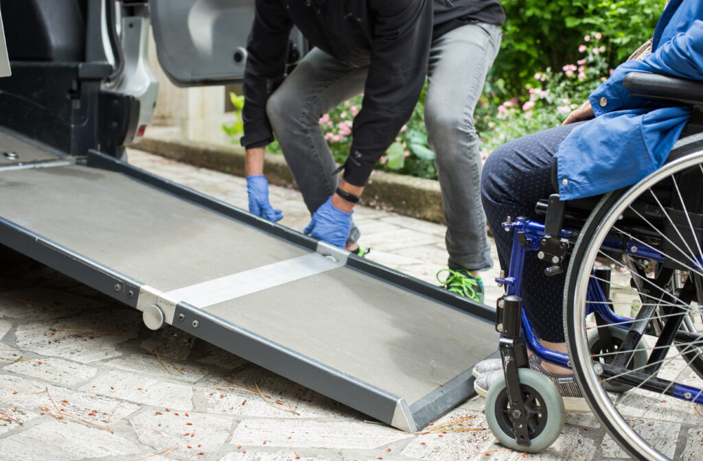 Caregiver adjusting wheelchair ramp for disabled individual to enter van.