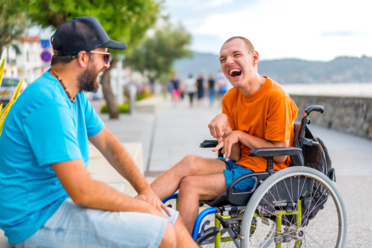 Young man with intellectual disability in a wheelchair enjoying a day by the seashore with family caregiver.