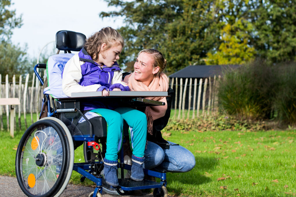 Intellectually disabled child in a wheelchair enjoying a stroll with caregiver.