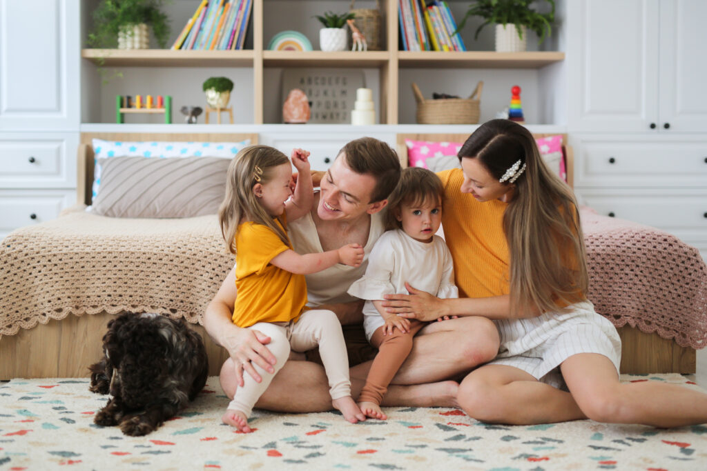 Happy family with down syndrome child and sibling sitting together on rug laughing.