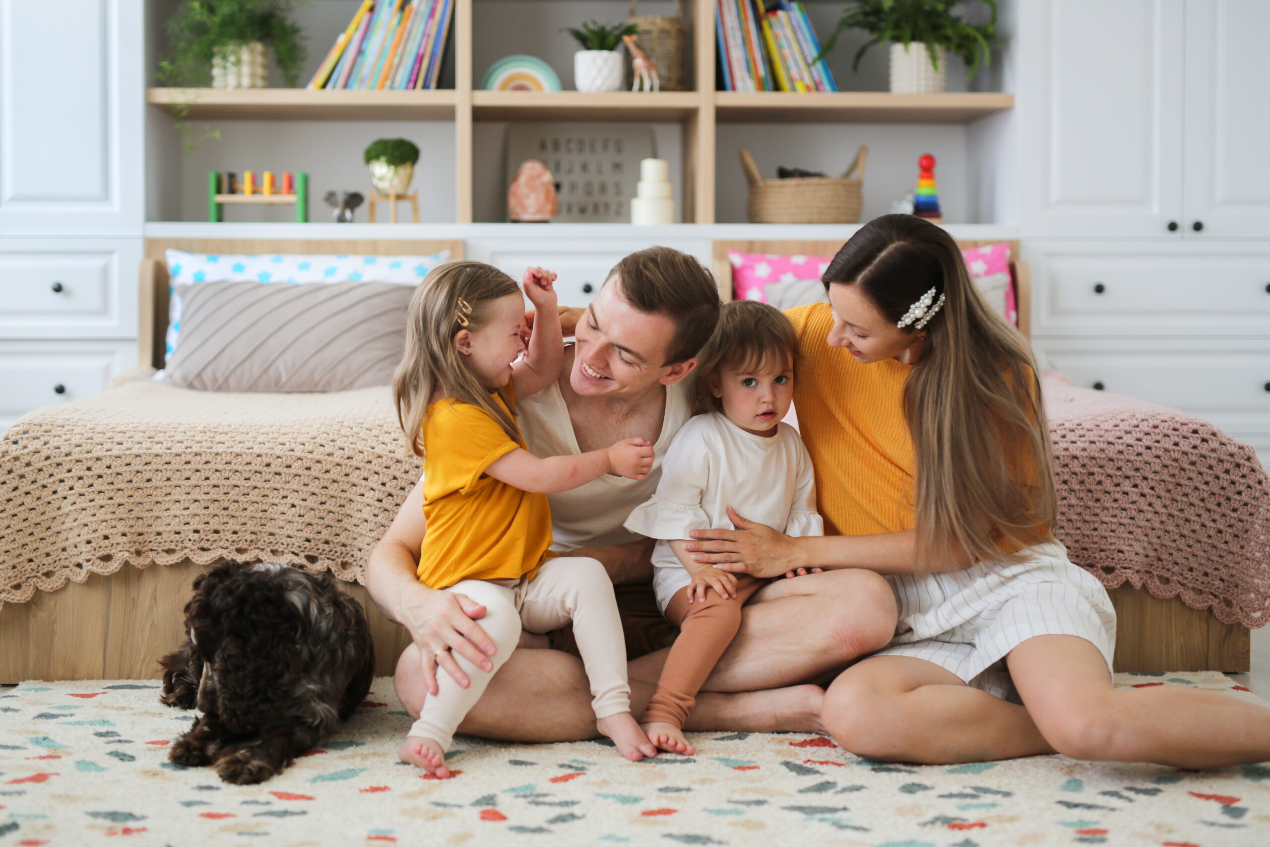 Happy family with down syndrome child and sibling sitting together on rug laughing.