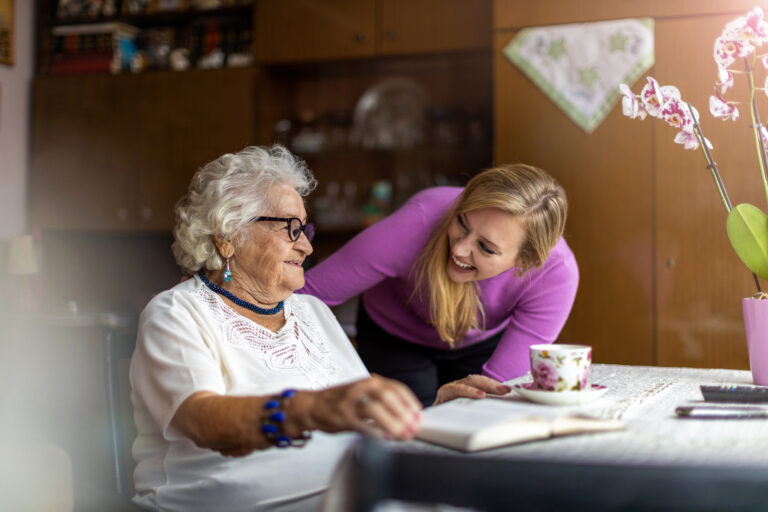 Senior woman sitting at table enjoying tea with family caregiver.