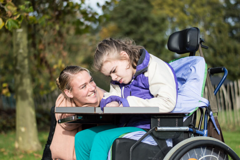 Disabled girl in a wheelchair relaxing outside with caregiver.