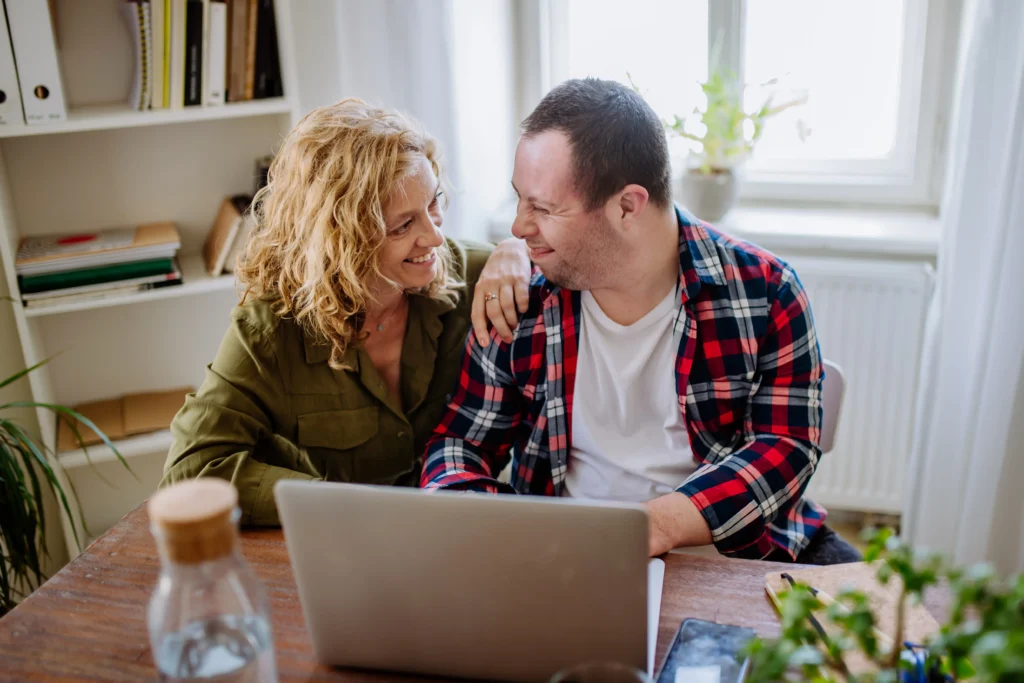 Adult man with developmental disabilities using computer with the help of his sister.